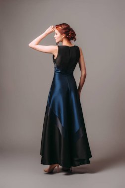 Donanma uzun gece elbisesi. Yüksek topuklu ayakkabı giyen güzel bir manken, modern kadınsı bir etkinlik arıyor. Klasik kadın modası. Sevimli kızıl kadın..