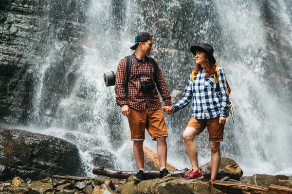 Man and woman hikers trekking a rocky path against the background of a waterfall and rocks. Hiker couple exploring nature. — Stock Photo, Image