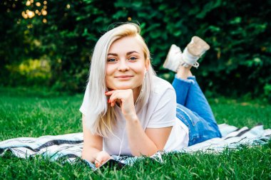 Kulaklıklı, akıllı telefonlu güzel sarışın kız yeşil arka planda uzanan müziği dinliyor. Yaşam tarzı konsepti. Kopyala, metin için boşluk.