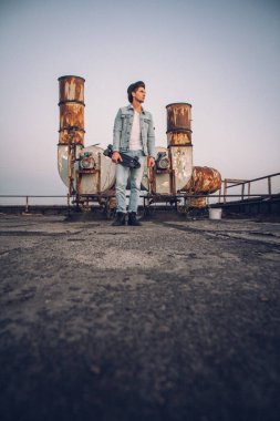 Şapkalı ve kaykaylı bir adam. Yakışıklısın. Havalı adam. Beyaz gömlek ve kot pantolon giyiyordu. Arka planda eski ihmal edilmiş bina.