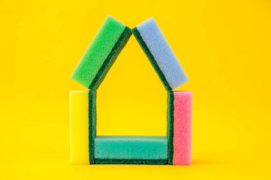 Sarı arka planda ev şeklinde katlanmış temizlik için çok renkli süngerler. Metin için boşluk.
