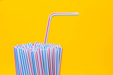 Sarı arka planda plastik pipet içmek. İçme suyu veya meşrubat için kullanılan plastik pipetlerle dolu. Seçici odaklanma. Boşluğu kopyala.