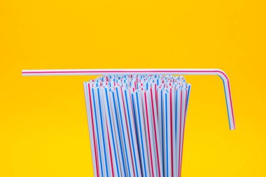 Sarı arka planda plastik pipet içmek. İçme suyu veya meşrubat için kullanılan plastik pipetlerle dolu. Seçici odaklanma. Boşluğu kopyala.