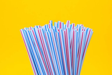 Sarı arka planda plastik pipet içmek. İçme suyu veya meşrubat için kullanılan plastik pipetlerle dolu. Seçici odaklanma. Boşluğu kopyala.