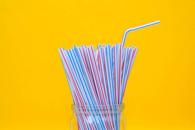 Sarı arka planlı cam bir kavanozda plastik pipetler. Metin için boşluk.