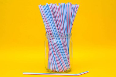 Sarı arka planlı cam bir kavanozda plastik pipetler. Metin için boşluk.