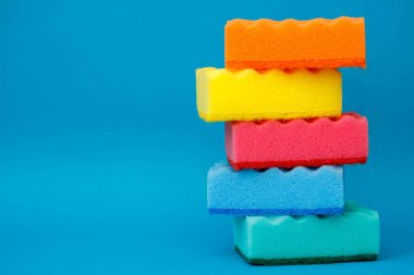 Mavi arka planda bulaşık yıkamak ve temizlemek için çok renkli süngerler. Metin için boşluk.