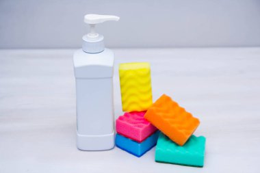 Beyaz bir masada bulaşık yıkamak için plastik şişe ve sünger. Temizlik malzemeleri. Metin için boşluk.