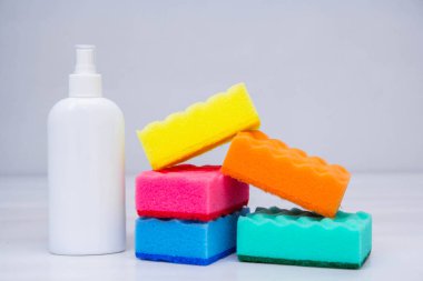 Bulaşık yıkamak için çok renkli süngerler ve beyaz bir masada plastik şişe. Temizlik malzemeleri. Metin için boşluk.