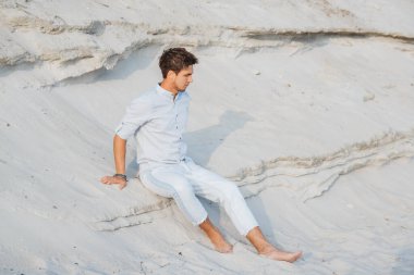 Hafif giysili genç yakışıklı çölde oturuyor. Özgürlük rahatlama kavramı. Metin veya reklam için yer.