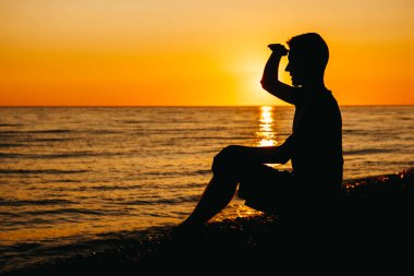 Deniz arka planında ve gün batımında sahilde oturup düşünen bir adamın silueti. Özgürlük rahatlama kavramı. Metin veya reklam için yer.
