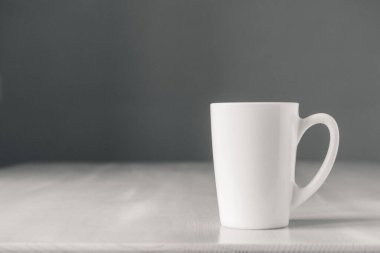 Beyaz seramik bardak beyaz ahşap masa üzerinde gri arka planda. Metin veya reklam için yer.