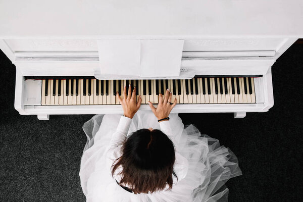 Красивая женщина в белом платье играет на белом пианино. Вид сверху.