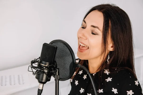 Portrait of beautiful woman sings a song near a microphone in a recording studio. Place for text or advertising.