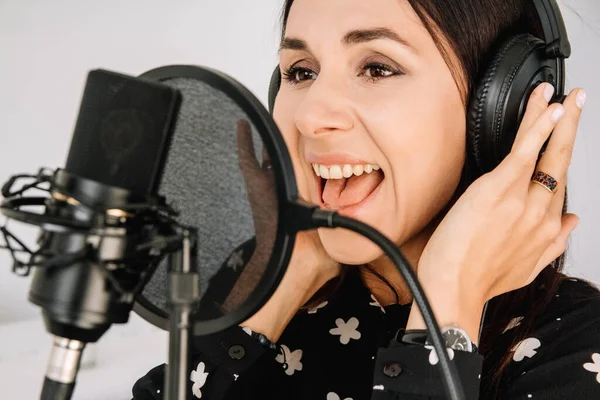 Portrait of beautiful woman in headphones sings a song near a microphone in a recording studio.. Place for text or advertising.