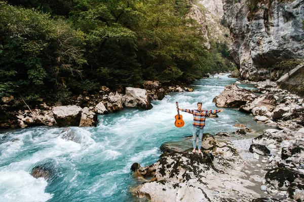 Hombre Sosteniendo Guitarra Pie Orilla Río Montaña Sobre Fondo Rocas — Foto de Stock