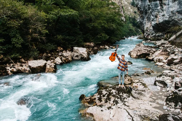 Hombre Sosteniendo Guitarra Pie Orilla Río Montaña Sobre Fondo Rocas — Foto de Stock