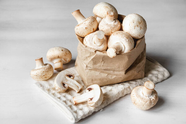 Mushrooms champignons in paper bag on a white wooden table. Place for text or advertising.