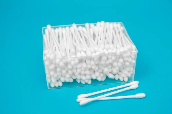 Cotton buds in plastic transparent rectangular container and several cotton buds separately on a blue background. Space for your text message or promotional content.