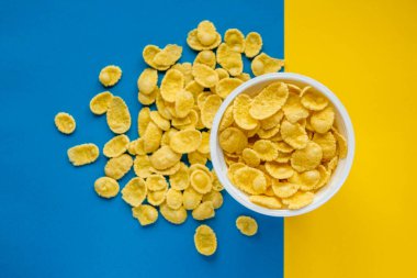 Mavi ve sarı arka planda beyaz kasede mısır gevrekleri. Üst Manzara. Kopyala, metin için boşluk.