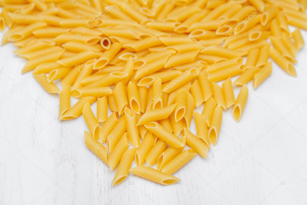 Pasta penne rigate on a white wooden table background. Top view, copy space.