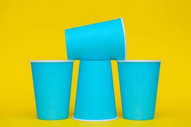 Sarı arka planda tek kullanımlık mavi bardaklar piramidi. Partiye hazırız. Kopyala, metin için boşluk.