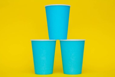Sarı arka planda tek kullanımlık mavi bardaklar piramidi. Partiye hazırız. Kopyala, metin için boşluk.