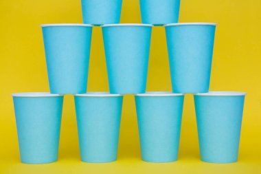 Sarı arka planda tek kullanımlık mavi bardaklar piramidi. Partiye hazırız. Kopyala, metin için boşluk.