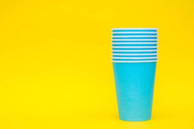 Sarı arka planda tek kullanımlık mavi bardaklar. Partiye hazırız. Kopyala, metin için boşluk.