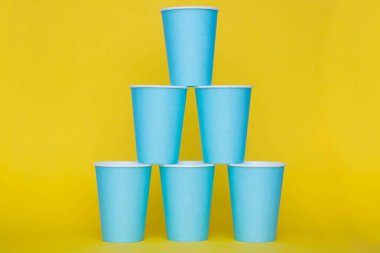 Sarı arka planda tek kullanımlık mavi bardaklar piramidi. Partiye hazırız. Kopyala, metin için boşluk.