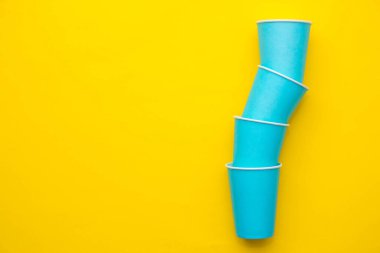 Sarı arka planda tek kullanımlık mavi bardaklar piramidi. Partiye hazırız. Kopyala, metin için boşluk.