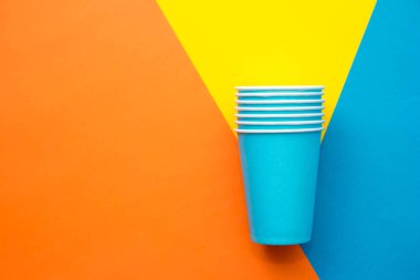 Çok renkli arka planda tek kullanımlık mavi bardaklar. Üst Manzara. Minimalist stil. Kopyala, metin için boşluk.