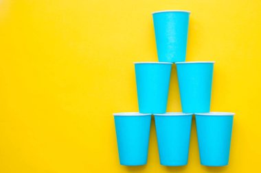 Sarı arka planda mavi kağıt bardaklar. Partiye hazırız. Üst Manzara. Minimalist stil. Kopyala, metin için boşluk.