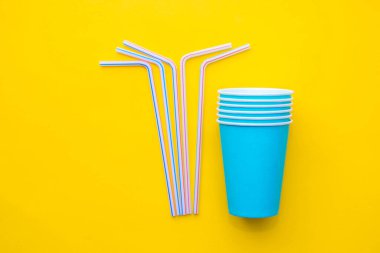 Sarı arka planda renkli plastik pipetler içen mavi kağıt bardaklar. Partiye hazırız. Üst Manzara. Minimalist stil. Kopyala, metin için boşluk.