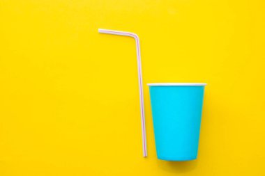 Sarı arka planda renkli plastik pipetler içen mavi kağıt bardaklar. Partiye hazırız. Üst Manzara. Minimalist stil. Kopyala, metin için boşluk.