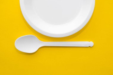 Plastik beyaz kaşık ve sarı arka planda plaka. Mutfak aletleri. Üst Manzara. Minimalist stil. Kopyala, metin için boşluk.