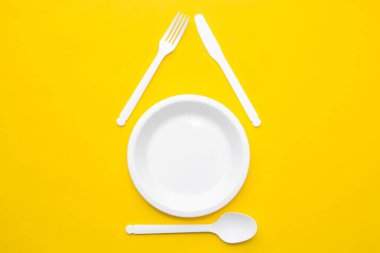Plastik beyaz çatal, bıçak, kaşık ve plaka sarı arka planda. Mutfak aletleri. Üst Manzara. Minimalist stil. Kopyala, metin için boşluk.