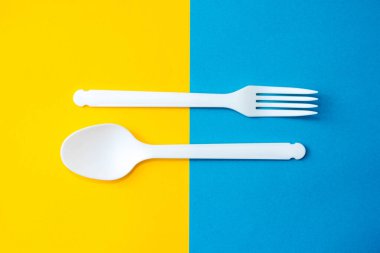 Sarı arka planda plastik beyaz kaşık ve çatal. Mutfak aletleri. Çatal bıçak seti. Üst Manzara. Minimalist stil. Kopyala, metin için boşluk.