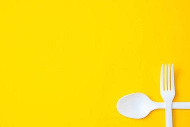 Plastik beyaz çatal ve sarı arka planda kaşık. Mutfak aletleri. Çatal bıçak seti. Üst Manzara. Minimalist stil. Kopyala, metin için boşluk.