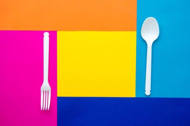 Çok renkli arka planda plastik beyaz çatal ve kaşık. Mutfak aletleri. Üst Manzara. Minimalist stil. Kopyala, metin için boşluk.