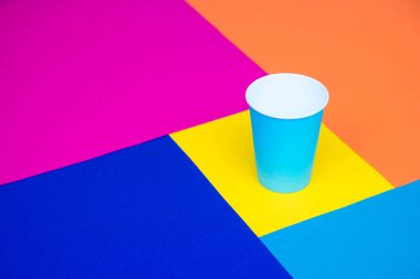 Çok renkli arka planda tek kullanımlık mavi kağıt bardak. Minimalist stil. Kopyala, metin için boşluk.