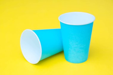 Sarı arka planda iki mavi kağıt bardak. Kopyala, metin için boşluk.