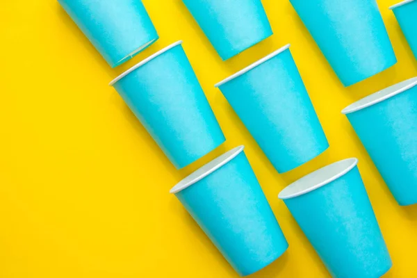 Pattern from blue paper disposable cups on yellow background. Set for party. Top view. Minimalist Style. Copy, empty space for text.