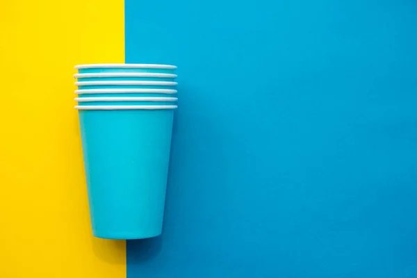 Pyramid of blue paper disposable cups on yellow background. Set for party. Copy, empty space for text.