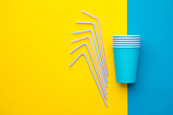 Blue paper cups with drinking colored plastic straws yellow and blue background. Set for party. Top view. Minimalist Style. Copy, empty space for text.