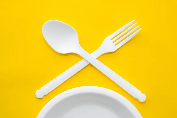 塑料白色叉子 勺子和盘子在黄色背景上 餐具的标志 顶部视图 简约主义风格 空的文字空间 — 图库照片