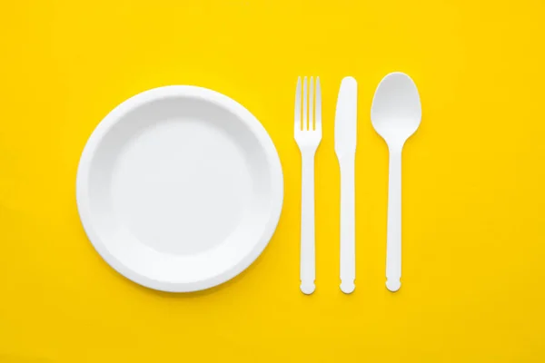 塑料白色叉子 勺子和盘子 黄色背景 顶部视图 简约主义风格 空的文字空间 — 图库照片