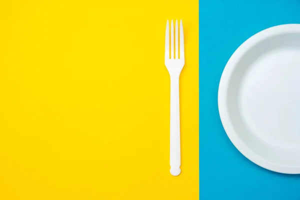 黄色和蓝色背景上的塑料白色叉子和盘子 顶部视图 简约主义风格 空的文字空间 — 图库照片