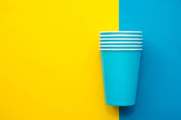Pyramid of blue paper disposable cups on yellow background. Set for party. Copy, empty space for text.