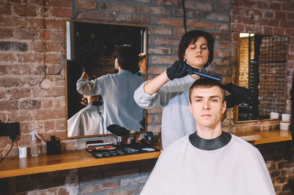 Beautiful woman hairdresser doing haircut to young man in barber shop. Advertising and barber shop concept.